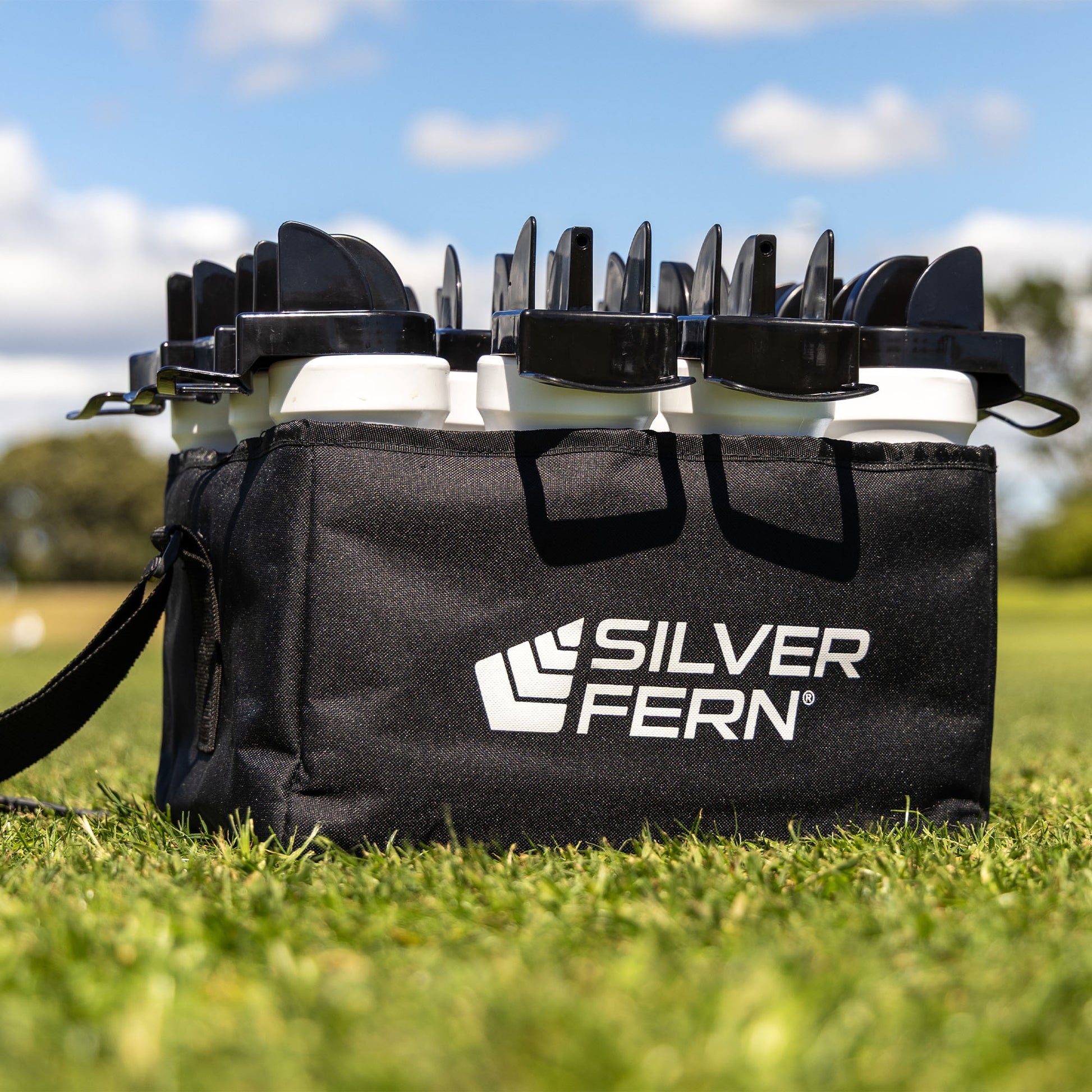 12-Pack Hygiene Bottles With Carrier, Drink Bottles with hygiene caps and chin holder for safe bottle sharing, 12-bottle fabric carrier with removable divider and adjustable carry strap / sling, lifestyle close-up shot, full pack sitting on the grass.